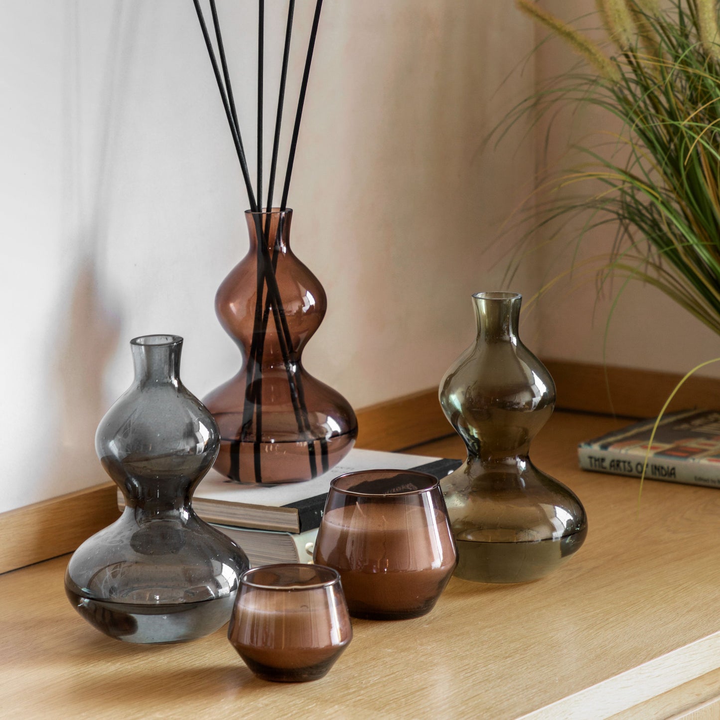 Brown glass reed diffuser with black reeds, featuring a sculptural curved silhouette and rose oud fragrance
