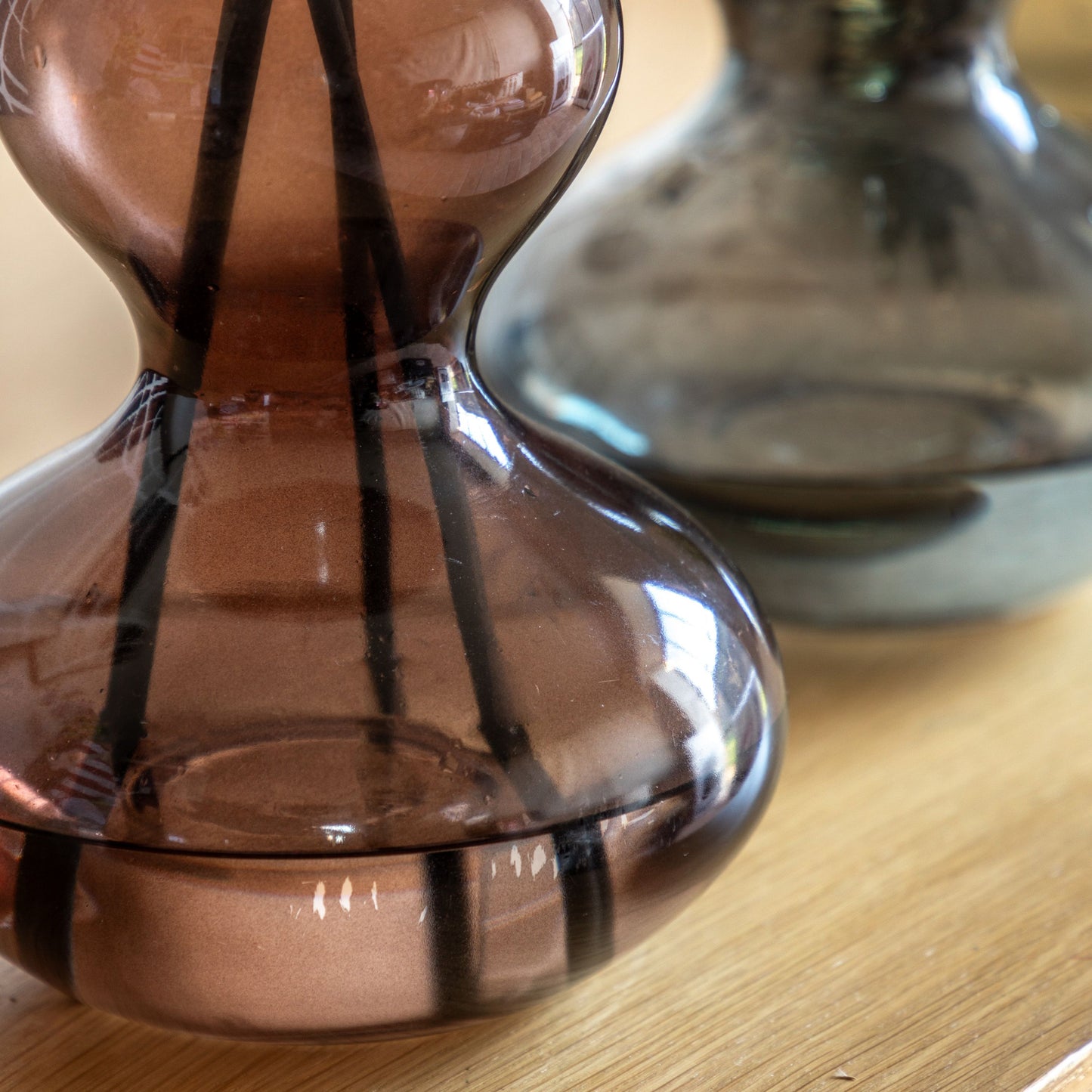 Brown glass reed diffuser with black reeds, featuring a sculptural curved silhouette and rose oud fragrance