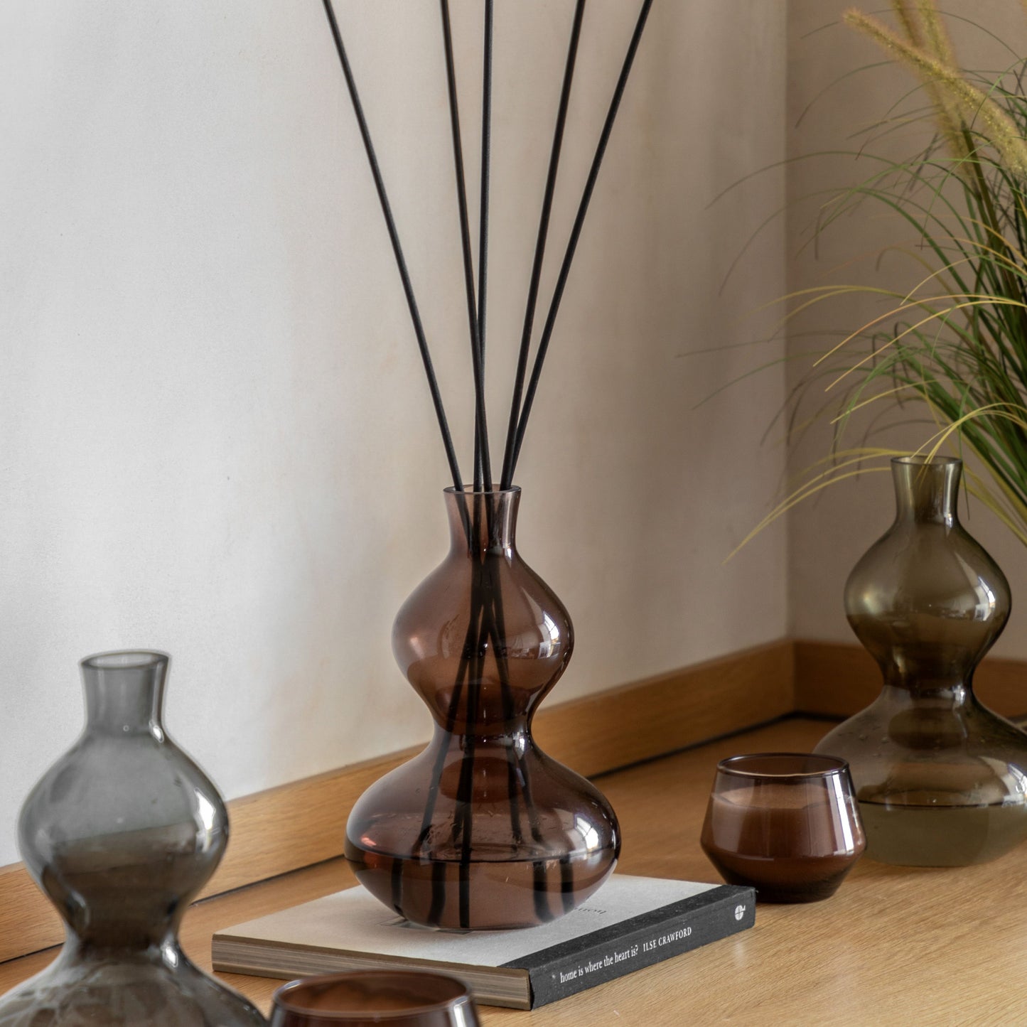 Brown glass reed diffuser with black reeds, featuring a sculptural curved silhouette and rose oud fragrance